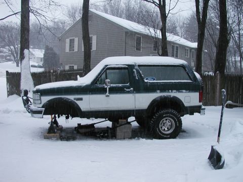 1994 Ford Bronco - A two-tone green and white 1994 Ford Bronco sits on jack stands in the snow, with its front wheels off.