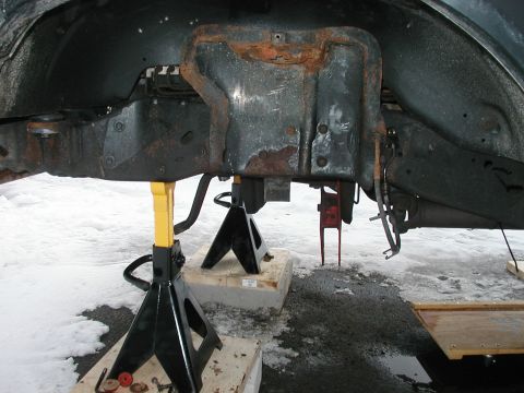 1994 Ford Bronco - Vehicle frame and suspension components are elevated on jack stands, revealing significant rust and wear.