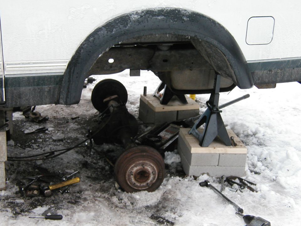Rear axle assembly on jack stands with tools on the ground in snow