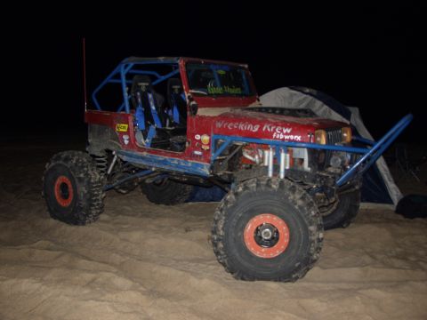 1979 Ford Bronco - Modified off-road vehicle with custom roll cage and large tires sits on sandy terrain near a tent.