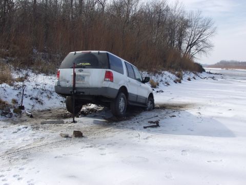 1979 Ford Bronco - A white SUV is stuck in the snow and ice, with a jack attempting to lift its rear wheel.