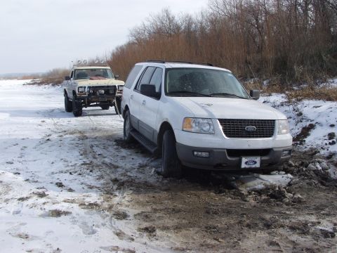 1979 Ford Bronco - Two Ford vehicles, a white Expedition and an older truck, are stuck in a muddy, snow-covered area.