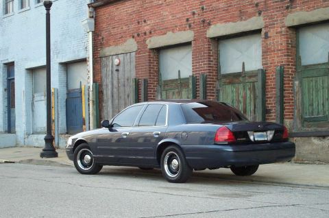 1998 Ford Crown Victoria - A dark blue sedan is parked on a street with a brick building behind it.