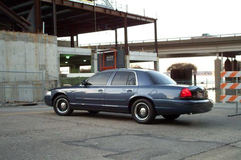 1998 Ford Crown Victoria - A dark blue sedan is parked near a construction site with a bridge overhead.