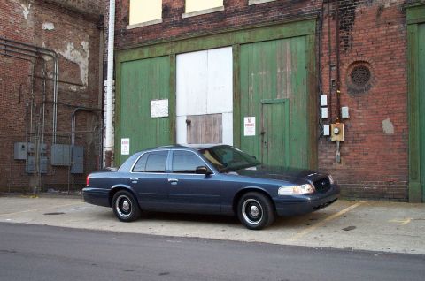 1998 Ford Crown Victoria - A dark blue sedan is parked in an alleyway in front of a large set of green doors.