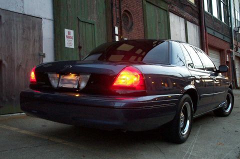 1998 Ford Crown Victoria - A dark sedan is parked in an alleyway with its brake lights illuminated.
