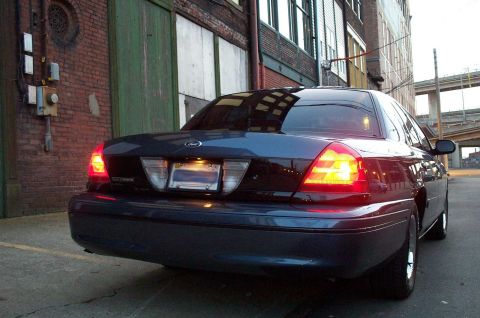 1998 Ford Crown Victoria - Rear view of a dark blue sedan parked next to a brick building.