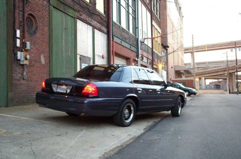 1998 Ford Crown Victoria - Dark 1998 Ford Crown Victoria parked on a city street with brick buildings.