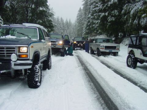 1986 Ford Bronco - Several off-road vehicles, including a 1986 Ford Bronco, navigate a snow-covered road.