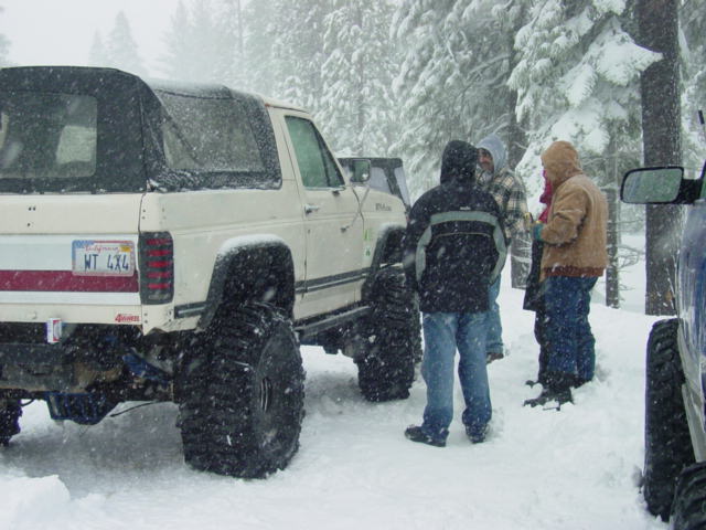 White off-road SUV with large tires parked in snow, people standing around it