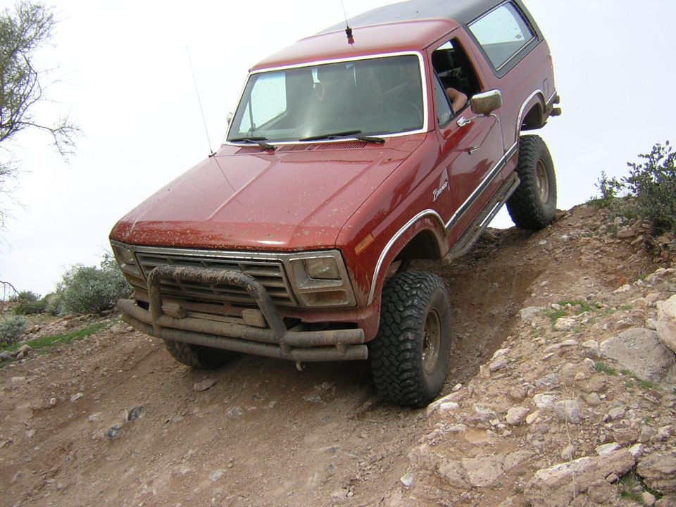 Red Ford Bronco with tube bumper climbing a rocky dirt embankment