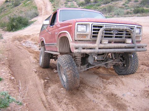 1984 Ford Bronco - A red Ford Bronco navigates a dusty, off-road trail with large tires.