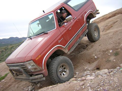 1984 Ford Bronco - A red Ford Bronco navigates a steep, rocky incline during an off-road excursion.