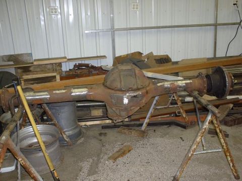 1978 Ford F-350 - A rusty rear axle assembly is supported by metal stands in a workshop setting, with various parts and materials in the background.