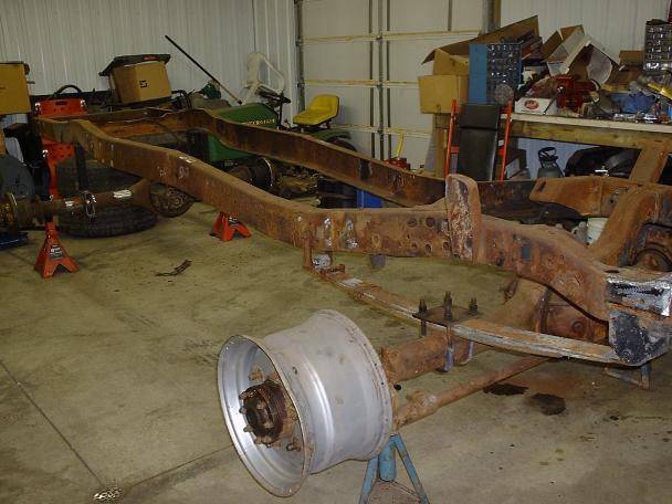 Rusted truck frame on jack stands in a garage, with a detached wheel in the foreground