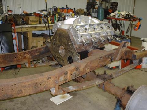 1978 Ford F-350 - A V8 engine is mounted on a heavily rusted truck chassis in a garage setting with tools and parts visible.