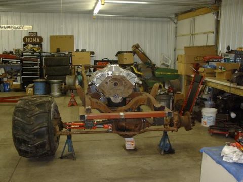 1978 Ford F-350 - A truck chassis, likely undergoing restoration or modification, is supported by stands in a workshop setting, with a large engine and a mas…