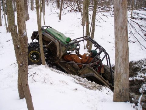 1992 Ford Bronco - An off-road buggy is tilted precariously in a snowy wooded area, with a driver visible inside.