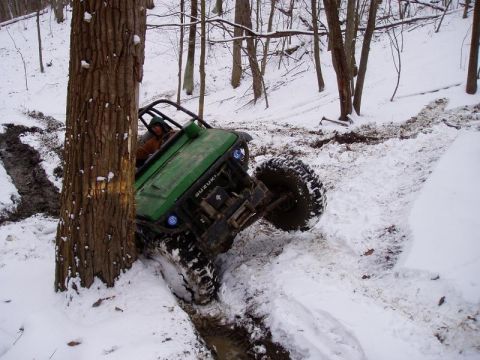 1992 Ford Bronco - Off-road vehicle navigates a challenging snowy terrain, getting stuck near a tree.
