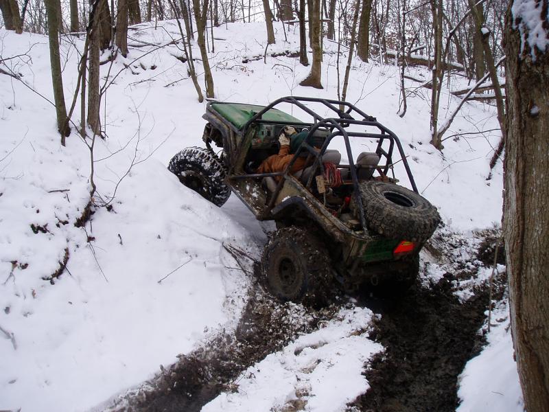 Green off-road vehicle with roll cage climbing snowy embankment