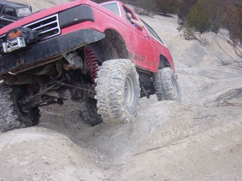 1983 Ford Bronco - A red SUV navigates a steep, sandy incline with another vehicle in the background.