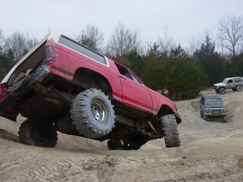 1983 Ford Bronco - Red 1983 Ford Bronco tackles an off-road obstacle, with two other SUVs visible on the trail.