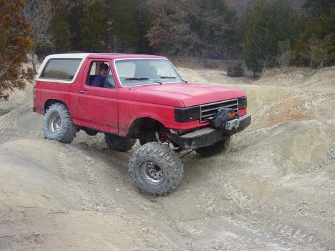 1983 Ford Bronco - A red Ford Bronco navigates a challenging off-road course with steep inclines and loose dirt.