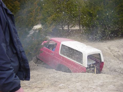 1983 Ford Bronco - A red and white 1983 Ford Bronco is stuck in the mud, with trees and debris in the background.