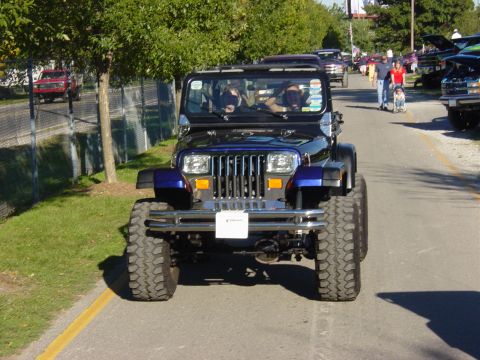 1983 Ford Bronco - Lifted Jeep Wrangler YJ driving on a sunny day with other vehicles present.