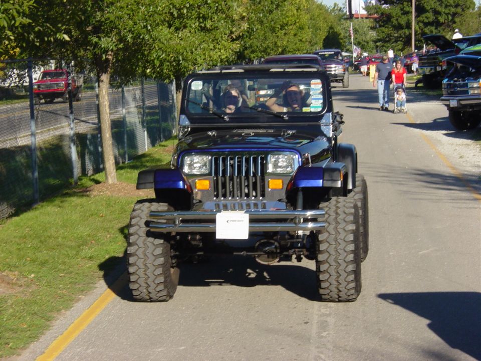 Lifted blue Jeep Wrangler YJ head-on at an outdoor 4x4 event on mud tires