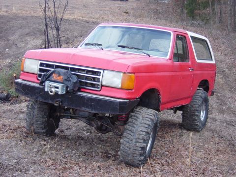 1983 Ford Bronco - This red SUV, likely a 1987 model, is equipped with oversized tires and a front-mounted winch for off-road use.