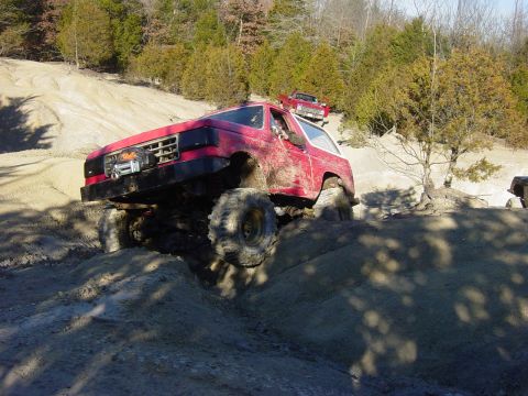 1983 Ford Bronco - A red off-road SUV navigates a challenging muddy terrain with another vehicle visible in the background.
