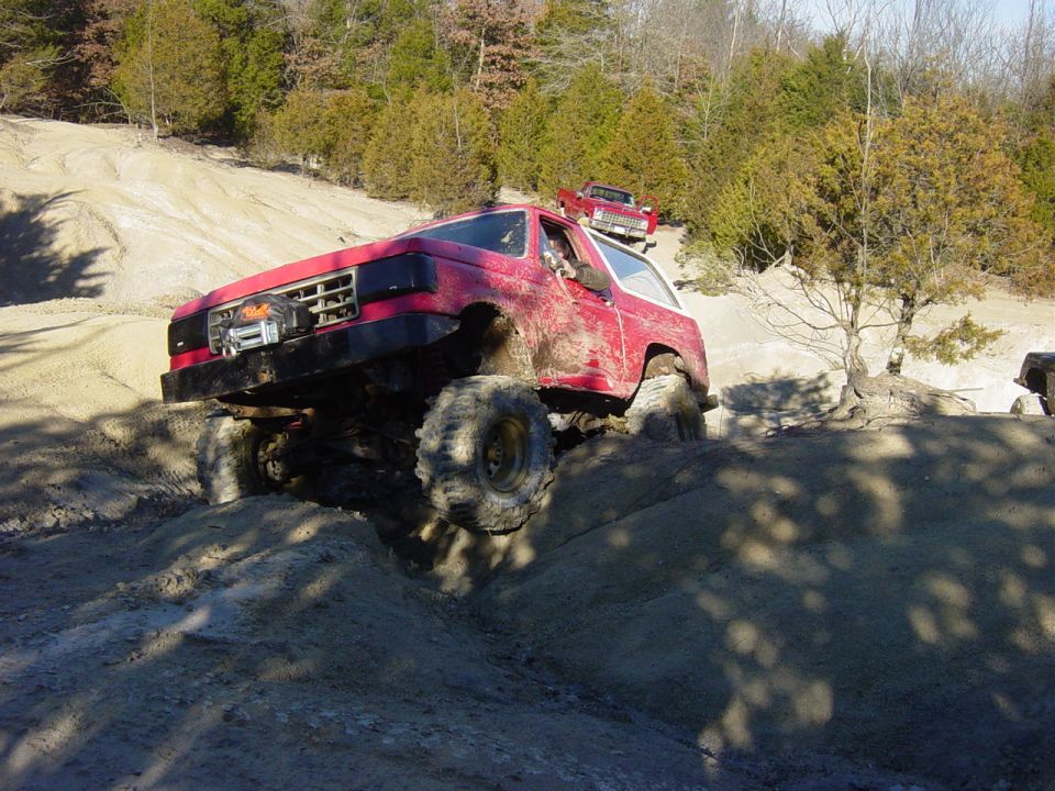 Red lifted Ford Bronco with winch bumper climbing a rutted clay bank