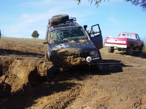 1983 Ford Bronco - A Jeep Cherokee is stuck in a mud pit while a red pickup truck attempts to pull it out.