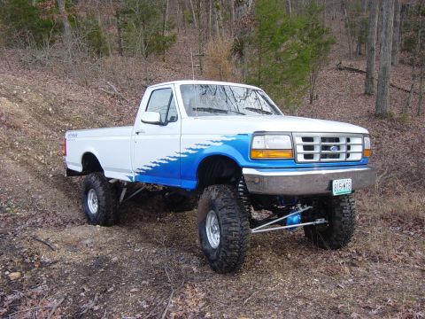 1983 Ford Bronco - This lifted Ford F-Series truck features a distinctive grille and blue flame decals, seen off-road.