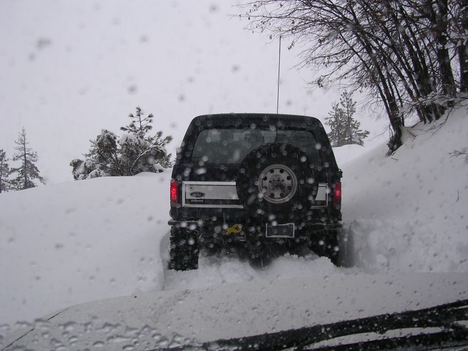 Black Ford Bronco driving through deep snow, rear view. Spare tire mounted on back