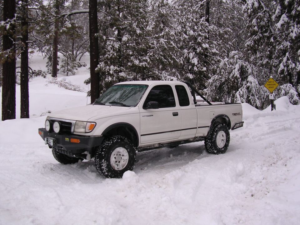 White 1999 Toyota Tacoma TRD 4x4 pickup truck driving in snow with trees in background