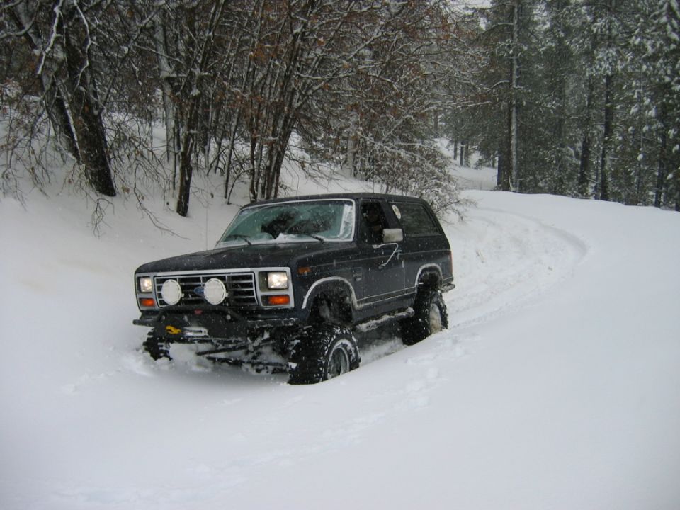 Dark blue Ford Bronco with large tires driving on a snowy road