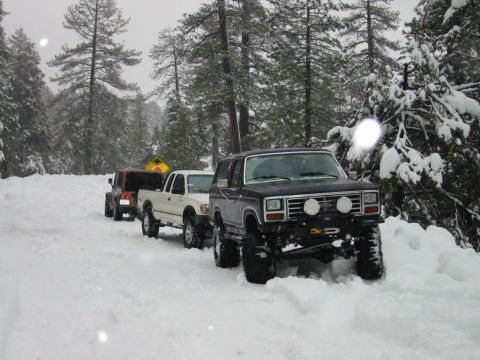 1999 Toyota Tacoma - Four-wheel drive vehicles navigate a snow-covered road through a forest.