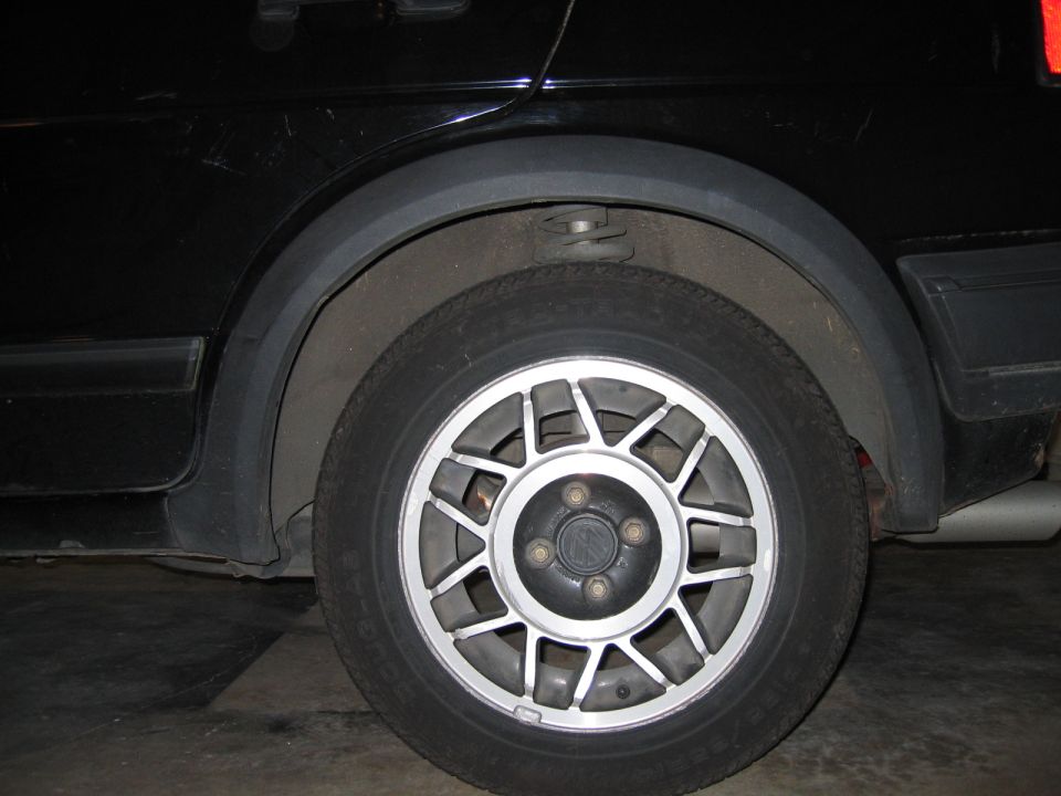 Rear alloy wheel and lower body of a black car shot in a garage