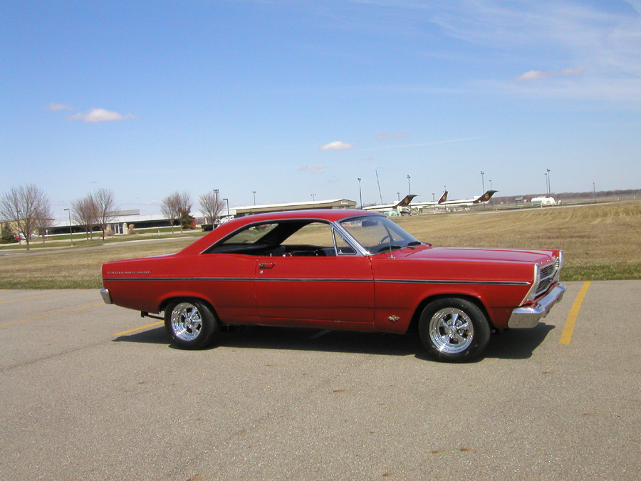 Red 1960s Ford Fairlane two-door hardtop parked on pavement, side profile