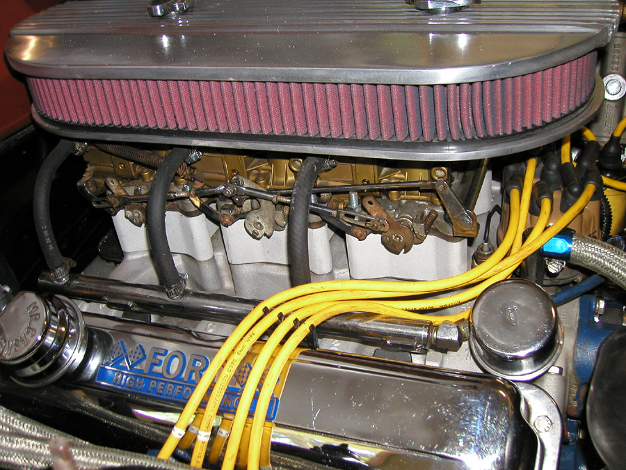 V8 engine with three carburetors, finned oval air cleaner, yellow plug wires, and chrome Ford valve cover