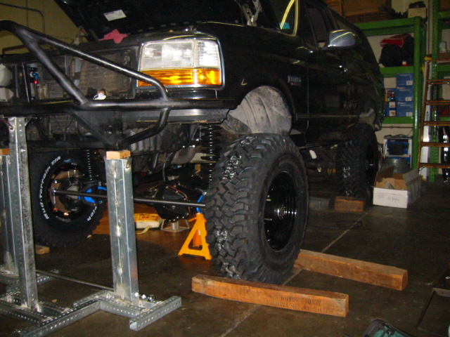 Black lifted Ford SUV on stands in garage mid solid-axle swap with hood open