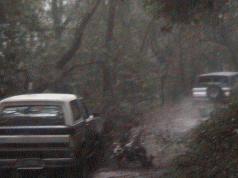 1991 Ford Bronco - Two SUVs navigate a dirt road surrounded by trees, with the lead vehicle appearing to be a 1991 Ford Bronco.