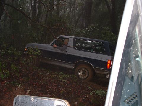 1991 Ford Bronco - A two-tone Ford Bronco navigates a muddy, wooded trail.
