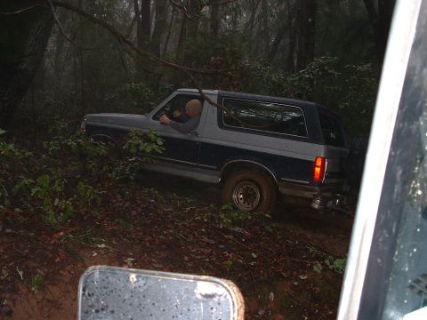 1991 Ford Bronco - A 1991 Ford Bronco navigates a muddy trail through a dense forest.