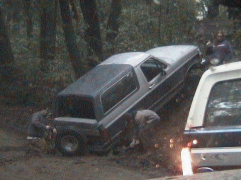 1991 Ford Bronco - Ford Bronco appears stuck in muddy terrain with assistance from bystanders.