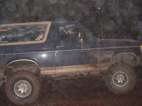 1991 Ford Bronco - Night flash photo of a mud-splattered dark blue and tan two-tone full-size Ford Bronco shot from the driver's side, sitting on a lift with…