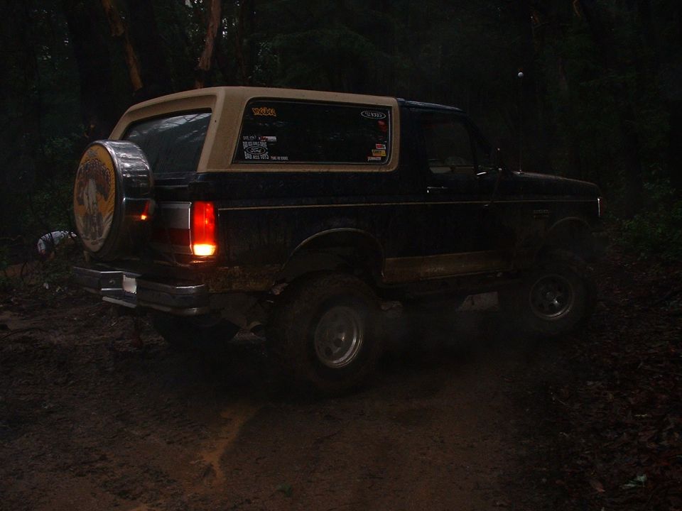 1991 Ford Bronco with a spare tire on the back, driving on a dirt road at night