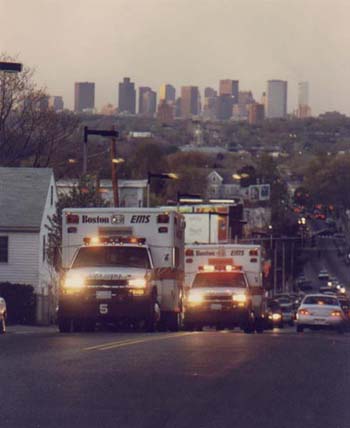 2000 Jeep Liberty - Two ambulances are parked on a street with a city skyline visible in the distance.